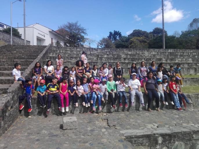 Niñas y niños del comedor infantil sentados en unas gradas durante una salida recreativa