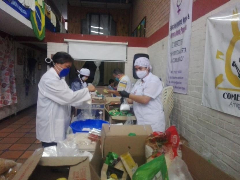 Voluntarias con bata y tapabocas empacando mercados